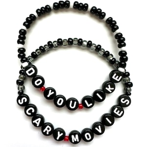 May include: Black and white beaded bracelet with the phrase "Do you like scary movies" spelled out in white letters on black beads. The bracelet has red accent beads.
