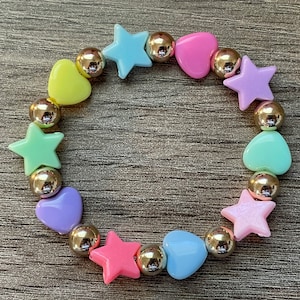 May include: A pastel-colored bracelet with alternating heart and star-shaped beads. The beads are made of plastic and are strung on a gold chain.