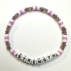 May include: A purple and white beaded bracelet with the word "STRENGTH" spelled out in white letter beads.