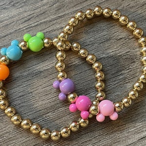 May include: Two gold beaded bracelets with colorful Mickey Mouse charms. The charms are in shades of green, blue, orange, purple, and pink.