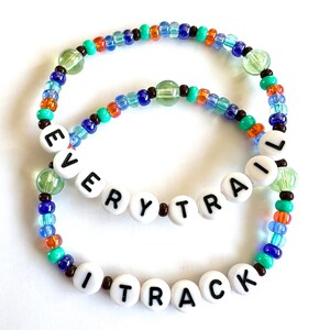 May include: Two beaded bracelets with the words "EVERY TRAIL I TRACK" spelled out in white letter beads. The bracelets feature a mix of colorful beads in shades of blue, green, orange, and brown.