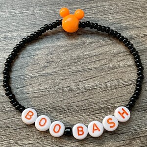 May include: A black beaded bracelet with white letter beads spelling "BOO BASH" and an orange Mickey Mouse head charm.