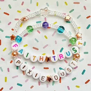May include: Two beaded bracelets with clear beads, gold stars, and white letter beads spelling "FAITH TRUST" and "PIXIE DUST".