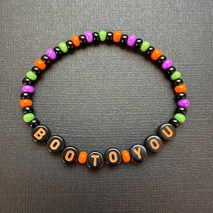 May include: A black beaded bracelet with orange, green, and purple beads spelling out "BOO TO YOU".