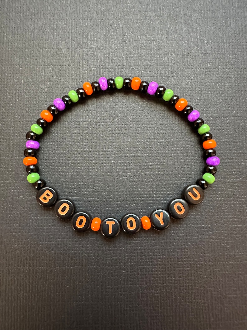 May include: A black beaded bracelet with orange, green, and purple beads spelling out "BOO TO YOU".