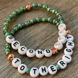 May include: Two green beaded bracelets with white letter beads spelling out "Second to the Right" and "Start Right".