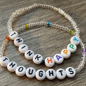 May include: White beaded bracelet with the words "Think Happy Thoughts" spelled out in colorful letters.