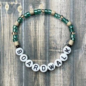 May include: A green and beige beaded bracelet with white letter beads spelling out "BOARDWALK".