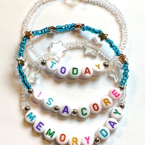 May include: Three beaded bracelets with the words "TODAY IS A CORE MEMORY DAY" spelled out in colorful letter beads. The bracelets feature clear, turquoise, and gold beads, with star-shaped and silver accents.