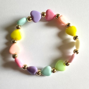 May include: A colorful bracelet featuring heart-shaped beads in pastel shades of pink, purple, yellow, green, and blue. The beads are interspersed with gold-colored spherical beads, creating a cheerful and playful accessory.
