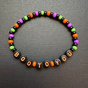 May include: A black beaded bracelet with orange, green, and purple beads spelling out "BOO TO YOU".