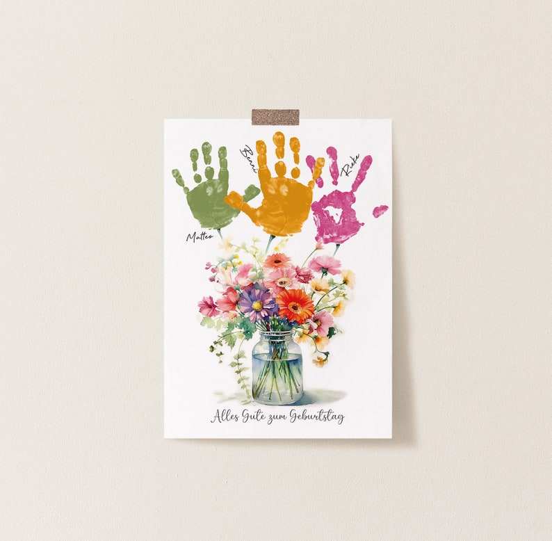 May include: A white card with three handprints in green, orange, and pink. The handprints are labeled with the names "Mattia", "Ben", and "Rika". A bouquet of flowers in a glass jar is below the handprints. The card says "Alles Gute zum Geburtstag" which is German for "Happy Birthday".