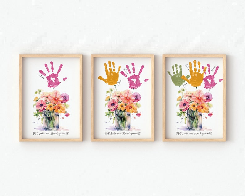 Op de afbeelding: Drie ingelijste prints met handafdrukken in verschillende kleuren, roze, oranje en groen, gerangschikt in een rij. Elke print toont een aquarel van een boeket bloemen in een glazen pot. De tekst "Mit Liebe von Hand gemacht" is onder elke afbeelding gedrukt.