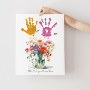 May include: A white card with a watercolor painting of a bouquet of flowers in a glass jar. The flowers are pink, orange, yellow, and purple. Two handprints are above the flowers, one yellow and one pink, with the names "Rike" and "Mattea" written next to them. The card says "Alles Gute zum Geburtstag" at the bottom.