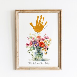 May include: A framed print with a yellow handprint, a bouquet of flowers in a glass jar, and the text "Alles Gute zum Geburtstag".