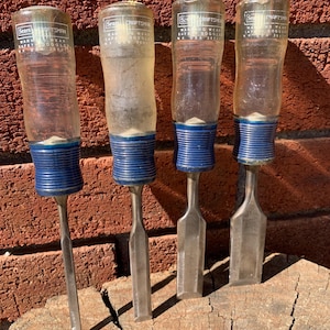 May include: Four Craftsman chisels with clear plastic handles and blue collars. The chisels have silver blades of varying shapes and are arranged on a weathered wooden surface. The handles have the Sears Craftsman logo.
