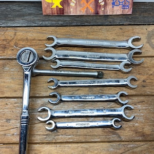 May include: A set of eight wrenches, including a Husky ratcheting wrench and seven Pittsburgh wrenches. The wrenches are silver and have various sizes, including 7/16, 1/2, 5/8, 3/4, 10, 12, and 6. The wrenches are arranged on a wooden surface.