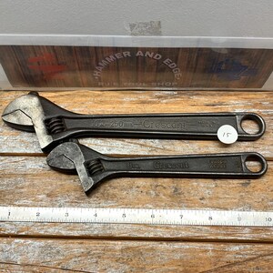 May include: Two black Crescent adjustable wrenches. The larger wrench is marked "10 in - 250 mm" and "Made in U.S.A.". The smaller wrench is marked "8 in". Both wrenches are on a wooden surface.