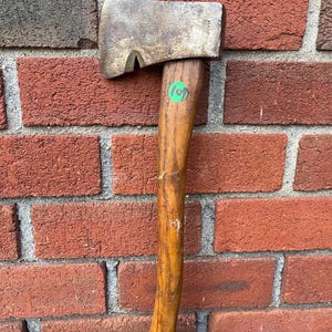 May include: A vintage metal hatchet with a weathered steel head featuring a distinct notch near the blade edge and a wooden handle. A small green circular sticker with the number 109 is affixed to the upper portion of the handle.