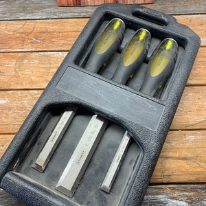 May include: A set of three Stanley chisels in a black plastic case. The chisels are yellow and black with the Stanley logo on them. The case has a handle and a Stanley logo on the side.