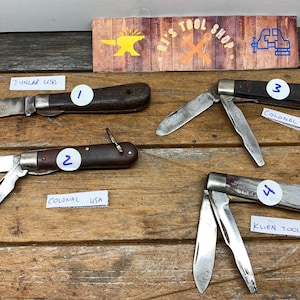 May include: Four pocket knives with wooden handles. The knives are labeled 1, 2, 3, and 4. The knives are on a wooden surface. The knives are all closed. The knives are all different brands. The knives are all different sizes. The knives are all different colors. The knives are all different styles.