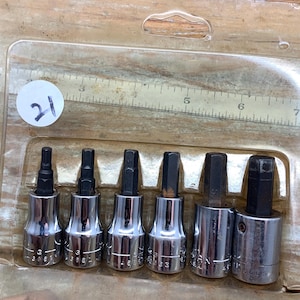 May include: A set of six hex bit sockets in a clear plastic package. The sockets are made of silver metal and black hex bits. The package has a ruler printed on it and a white sticker with the number 21.