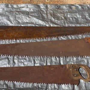 May include: Three vintage hand saws with rusted metal blades and wooden handles. The top saw features two wooden handles at each end, while the middle and bottom saws have single closed-loop wooden handles. All blades show significant oxidation.