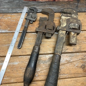 May include: Three vintage adjustable wrenches with wooden handles. The wrenches are made of metal and have a silver finish. The handles are brown and have a worn look.