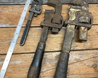 Puede incluir: Tres llaves inglesas ajustables vintage con mangos de madera. Las llaves son de metal y tienen un acabado plateado. Los mangos son marrones y tienen un aspecto desgastado.