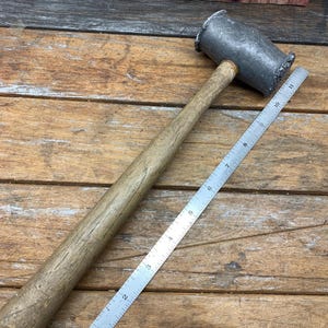 May include: A wooden-handled metal mallet with a rounded head. The mallet is approximately 17 inches long. The head of the mallet is made of a silver-colored metal and has a slightly textured surface.
