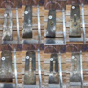 May include: A collection of eight vintage metal plane blades, each with a unique shape and wear pattern. The blades are arranged on a wooden surface with ruler markings, showcasing their size and condition. Numbers 20 through 27 are visible on the blades.