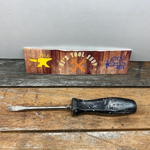 May include: A black and silver flathead screwdriver with a black plastic handle. The handle has the text "Snap-on" and "5004 USA" printed on it.