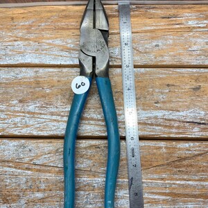 May include: A pair of Channellock 349 pliers with blue handles, next to a ruler. The pliers are marked "MEADVILLE, PA, USA". A white tag with the number 60 is attached. The ruler shows measurements in inches.