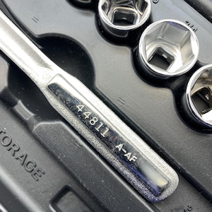 May include: A set of chrome sockets and a ratchet wrench are arranged in a black storage case. The wrench has the number "44811 A-AF" printed on it. The sockets are various sizes and shapes.
