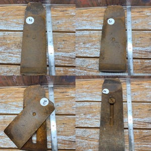 May include: Four antique, rusty metal woodworking plane blades. Each blade is a rectangular shape with a rounded top and a hole in the center. The blades are numbered 29, 30, 31, and 32. The blades are on a wooden surface.