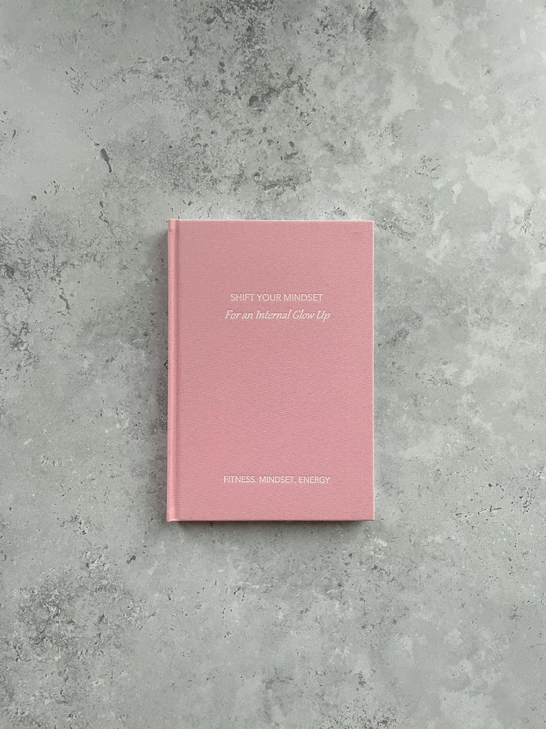 May include: A pink journal with the text "Shift Your Mindset For an Internal Glow Up" and "Fitness. Mindset. Energy" on the front cover.