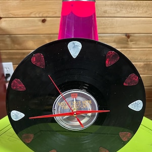 Könnte beinhalten: Eine schwarze Schallplattenuhr mit roten und weißen Plektren als Markierungen. Die Uhrzeiger sind rot, und das Zifferblatt trägt den Text "Rave With The Tray Cats". Ein dekorativer Artikel im Retro-Stil.