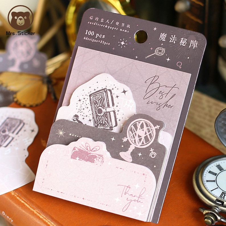 May include: A pack of 100 decorative memo notes with a magical theme. The notes feature illustrations of a book, a globe, a gift, and the text "Best wishes" and "Thank you".