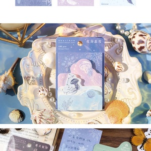 May include: A set of 100 decorative paper stickers with a variety of designs, including jellyfish, stars, snowflakes, butterflies, and planets. The stickers are packaged in clear plastic bags with a blue and white background. The text on the bags reads "夜海暮雪" and "魔法秘陣".