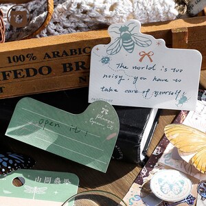 May include: A set of decorative stickers featuring a bee, a ladybug, a butterfly, and a dragonfly. The stickers are on a white background with green and blue accents. The stickers have text that reads "The world is too noisy, you have to take care of yourself!" and "Please open it!"