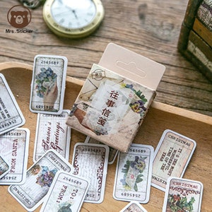 Könnte beinhalten: Ein Set Vintage-Weihnachtsaufkleber mit floralen Designs, handschriftlichem Text und den Worten "Season's Greetings" und "Christmas". Die Aufkleber sind in einer kleinen Schachtel mit dem Text "往事信笺" in Chinesisch verpackt.