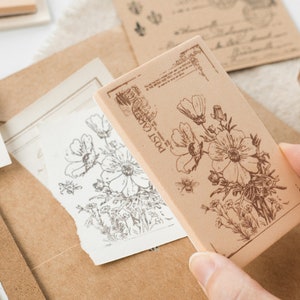 Op de afbeelding: Een bruine rubberen stempel met een vintage postkaartontwerp met een bloemenmotief en de tekst "POST CARD".