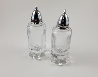 May include: A set of two clear glass salt and pepper shakers with silver tops and a beaded base.