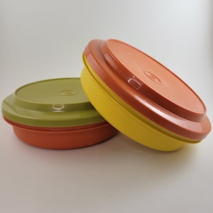 Puede incluir: Dos recipientes redondos de plástico con tapas. El recipiente superior es amarillo, naranja y verde. El recipiente inferior es naranja y verde.