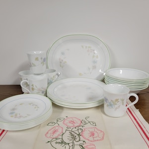 May include: A set of white Corelle dinnerware with a floral pattern in shades of blue, green, and pink. The set includes plates, bowls, and mugs.