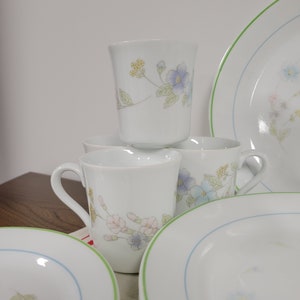 May include: A set of white ceramic mugs and plates with a floral design in shades of blue, pink, and green. The mugs have a handle and the plates have a green and blue rim.