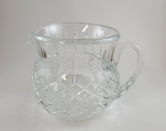May include: A clear glass pitcher with a diamond pattern. The pitcher has a handle and a wide mouth.