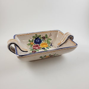 May include: A white ceramic serving dish with blue and yellow floral designs and two yellow handles.