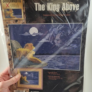 May include: A cross-stitch kit featuring a lion with a starry night sky and a full moon in the background. The kit includes 14 count navy Aida fabric, pre-sorted 6 strand cotton floss, a needle, a Soft Color Graph and instructions. The kit number is 03-134 K. The kit is manufactured and distributed by Janlynn Corporation.