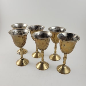 Puede incluir: Seis vasos de chupito de tono dorado con acabado martillado. Los vasos tienen una base redonda y un cuenco ancho y poco profundo.